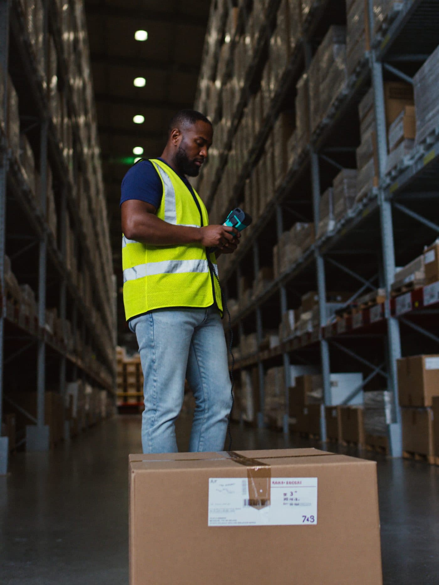 Warehouse worker scanning a barcode on a carton between tall storage racks