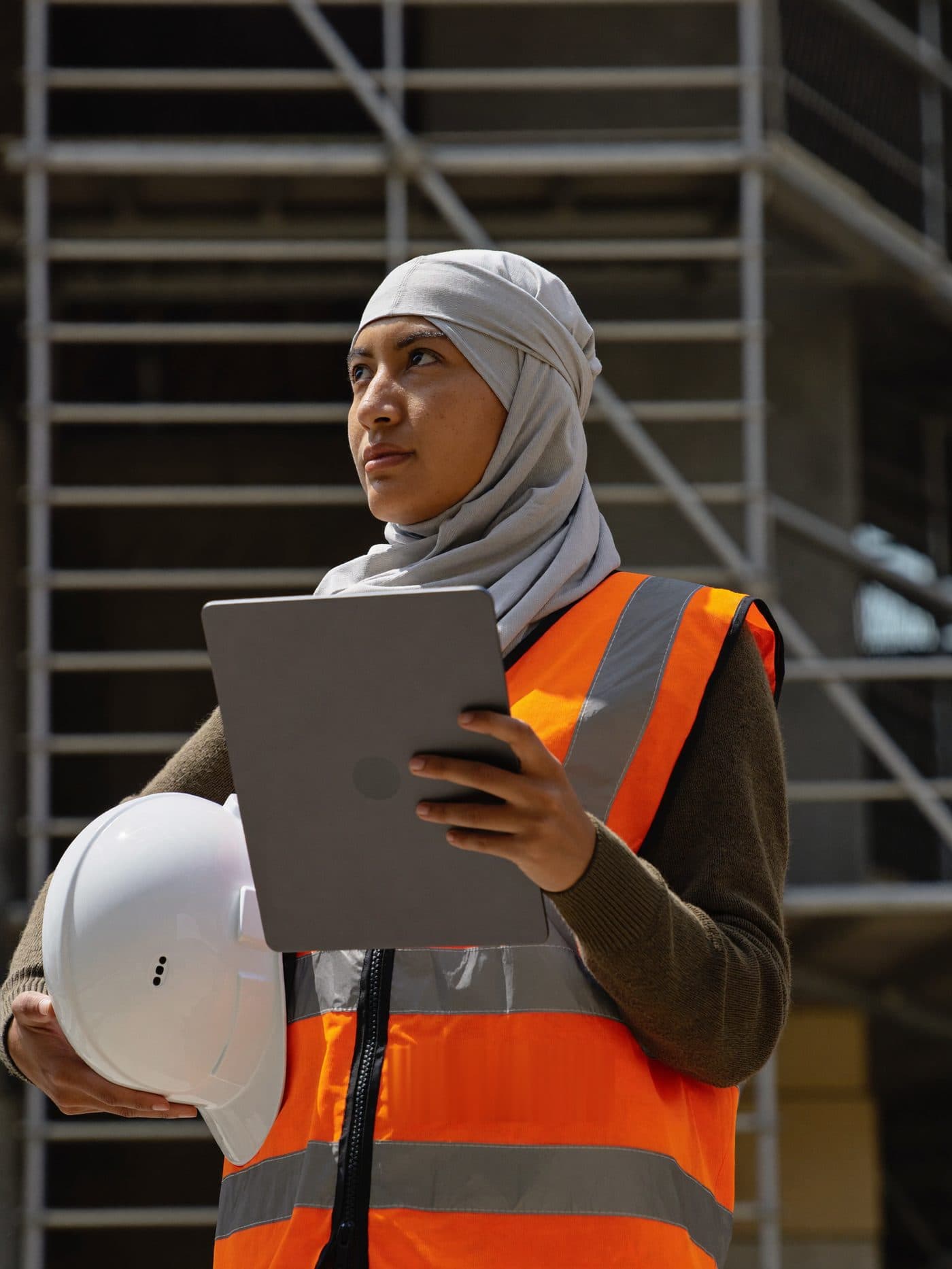 Site engineer in a hard hat reviewing progress on a tablet at a construction site